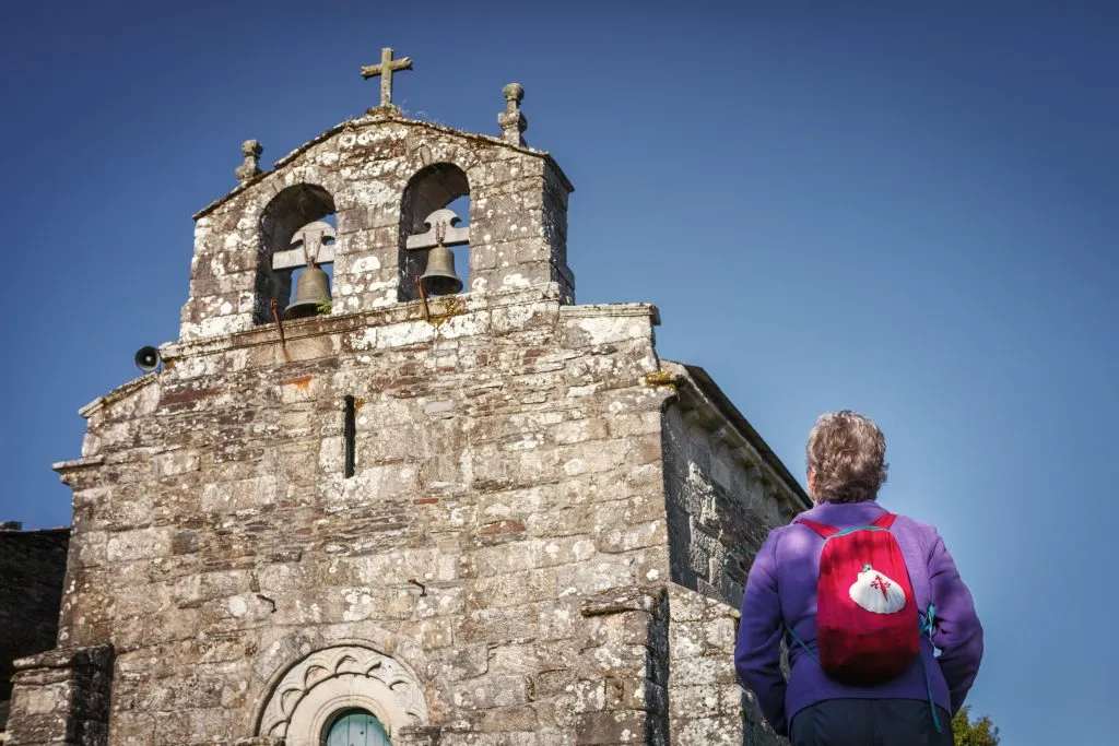 Auf dem Jakobsweg betrachtet ein Pilger die Schönheit der Kirche von Santiago in Baamonde, Spanien. Erbaut im 9. Jahrhundert bis zum 15. Jahrhundert.